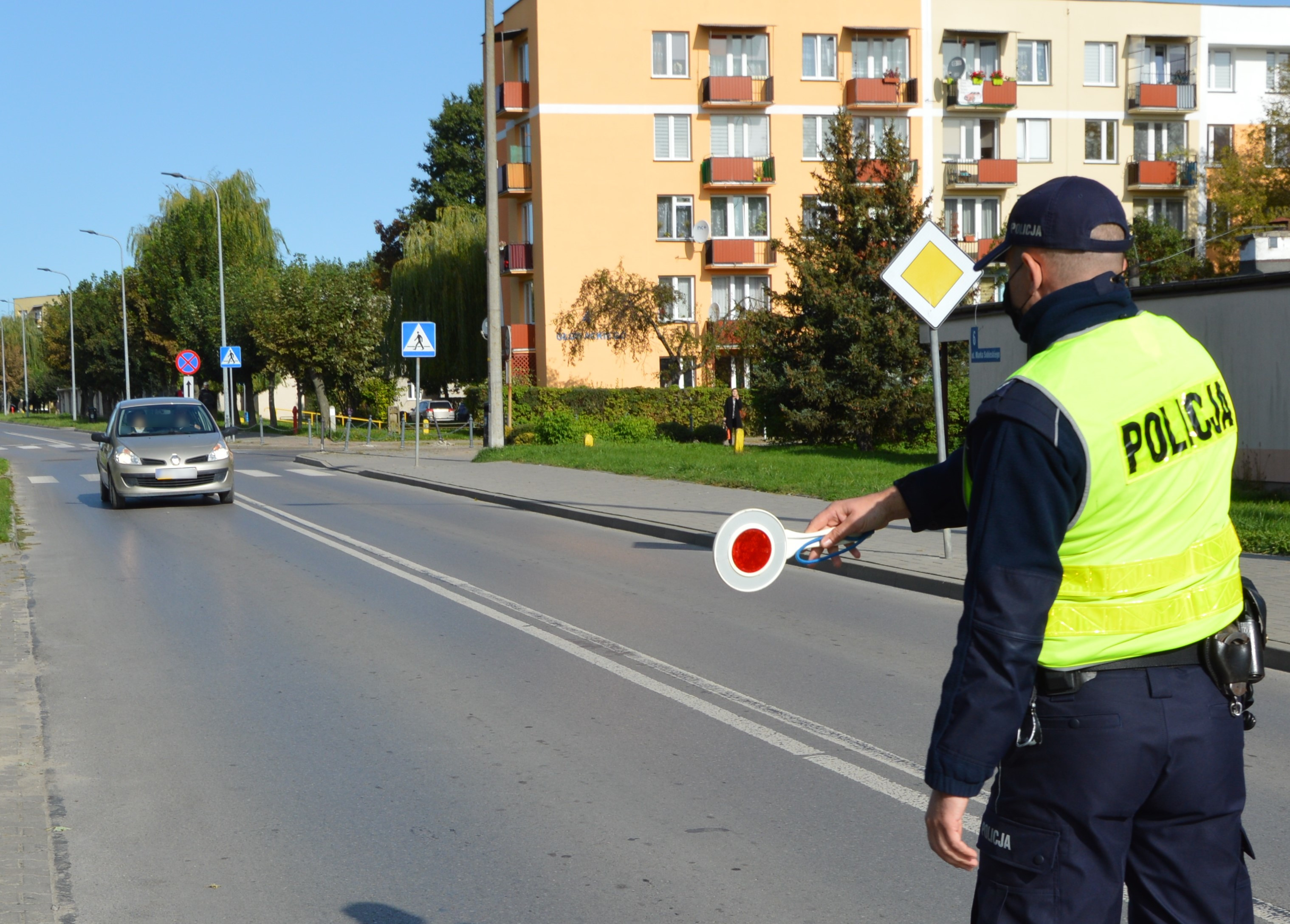 policjant zatrzymuje pojazd osobowy za pomocą tarczy do zatrzmywania pojazdów