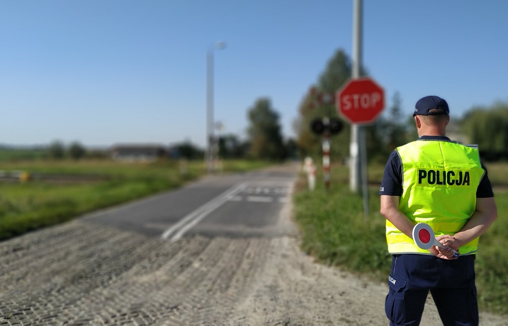 policjant stoi przed przejazdem kolejowym, w ręku trzyma tarczę do zatrzymywania pojazdów