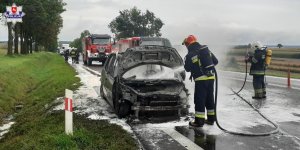 strażacy gaszą pożar samochodu stojącego na jezdi