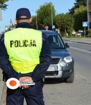 policjant stoi na zatoce, w ręku trzyma tarczę do zatrzymywania pojazdów