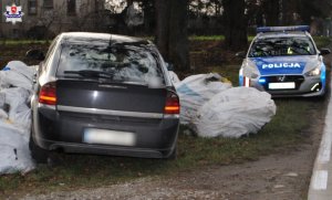 opel stojący na poboczu w workach z eternitem, obok stoi radiowóz policyjny