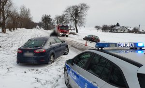 widoczny radiowóz policji, przed nim stoi na poboczu rozbity ford, a za nim na jezdni stoi radiowóz straży pożarnej