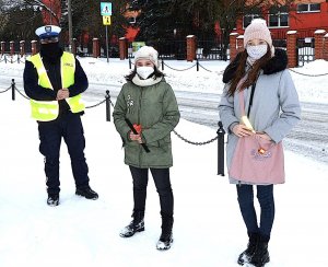 policjant i piesi uczestnicy ruchu drogowego trzymający w ręku elementy odblaskowe