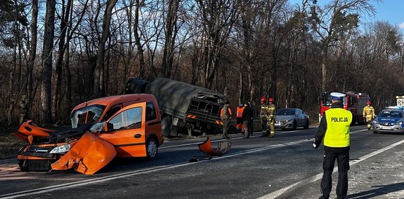 policjant na miejscu wypadku drogowego. W tle dwa samochody biorące udział wy wypadku