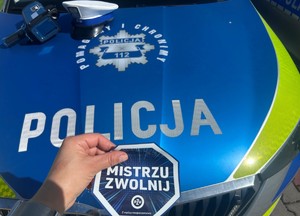 Ulotka kampanii Mistrzu Zwolnij trzymana w ręku na tle radiowozu