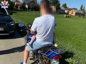 mężczyzna z dzieckiem na rękach siedzi na motorowerze