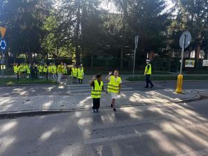 grupa dzieci ćwiczy przechodzenie przez jezdnię z policjantem