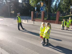 dzieci w kamizelkach odblaskowych przechodzą przez przejście dla pieszych w obecności policjanta