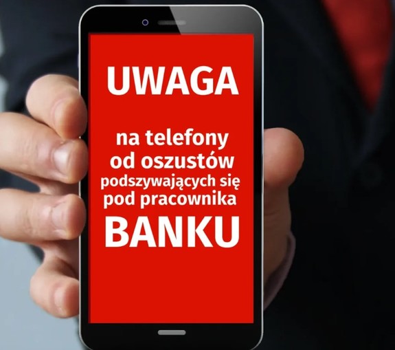 Telefon komórkowy trzymany w dłoni. Na ekranie wyświetlacza napis Uwaga na telefony od oszustów podszywających się pod pracownika banku.