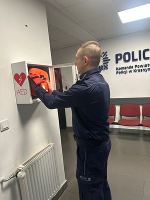 policjant umieszcza urządzenie AED w skrzynce