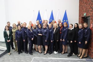 Grupa osób w Sali konferencyjnej uczestniczących w spotkaniu - kobiet i mężczyzn, policjantów i pracowników Policji. W tle flagi Polski i Unii Europejskiej.