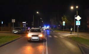 na lewym pasie ruchu za skrzyżowaniem i oznakowanym przejściem dla pieszych stoi samochód marki Skoda Fabia, obok stoi umundurowany policjant. Za skodą stoi oznakowany radiowóz policyjny.