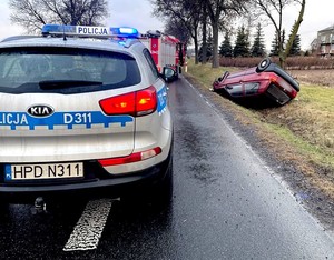 Radiowóz i przewrócony w rowie na dach pojazd osobowy.