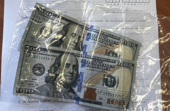 zabezpieczone dolary w folii, pod nimi policyjny protokół